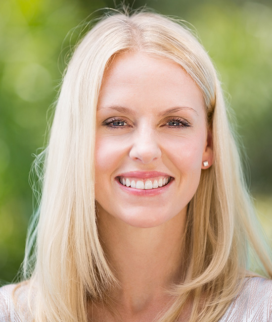 The image shows a woman with blonde hair and a friendly expression, smiling at the camera. She has short hair and is wearing what appears to be a light-colored top.