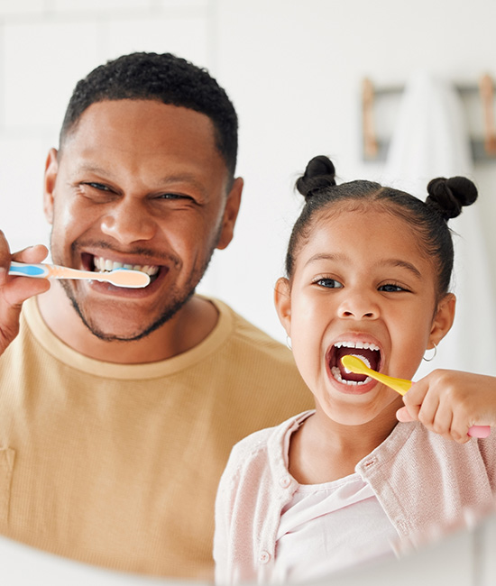 A man and a child brushing their teeth in front of a mirror.